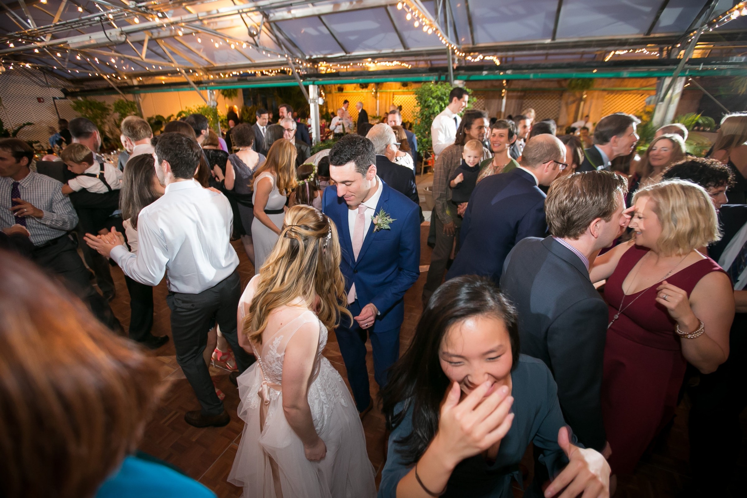 Bride and groom celebrating with guests under glowing string lights at Fairmount Park Horticulture Center.