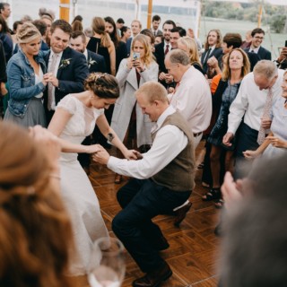 Bride and groom dancing joyfully surrounded by cheering guests at an outdoor farm wedding.