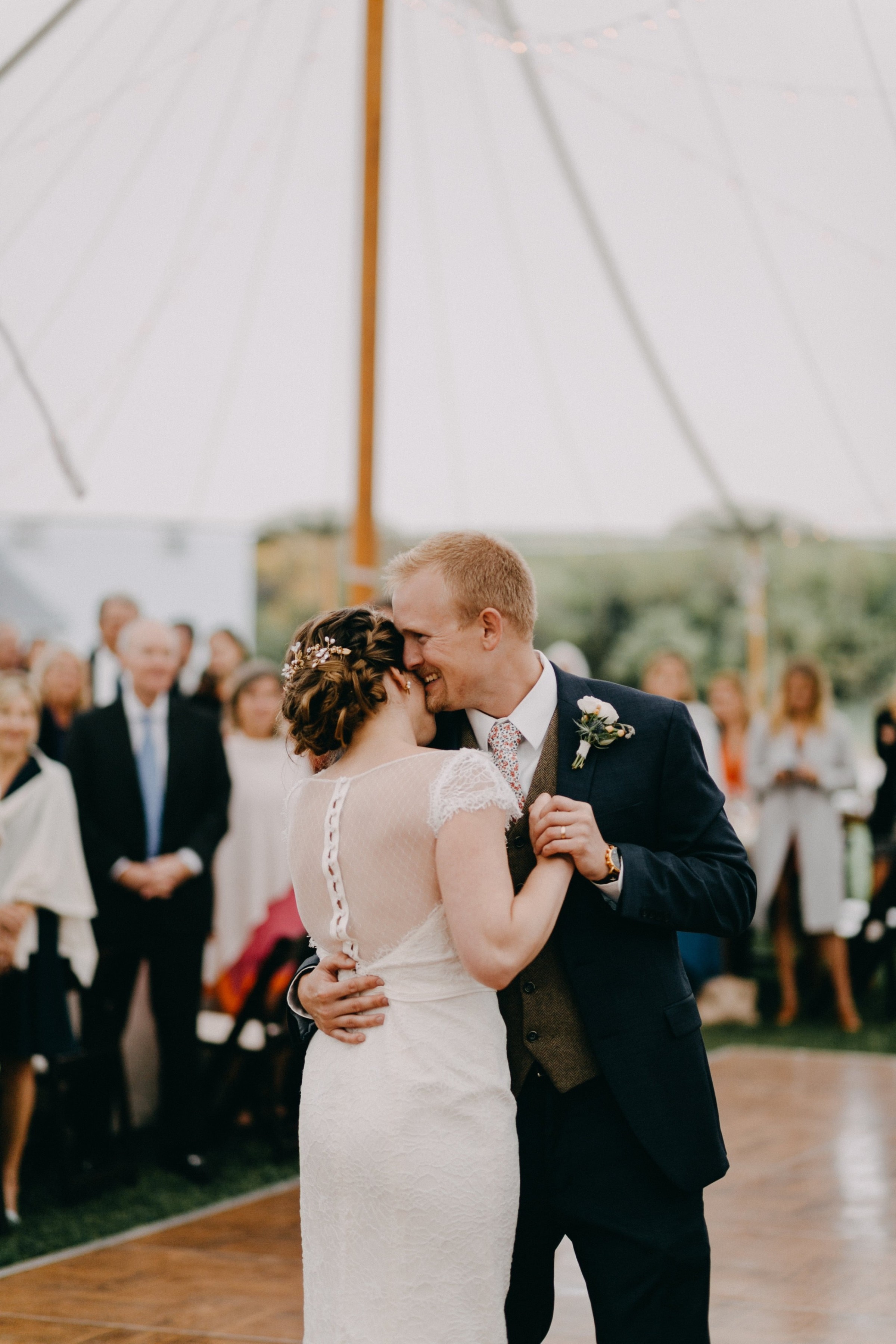 Bride and groom share a romantic first dance under a glowing tent at outdoor wedding.