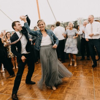 Couple dancing joyfully under white wedding tent surrounded by smiling guests in Newbury, Massachusetts.