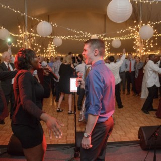 Couple singing at lively Waterville Valley wedding reception with dancing guests under warm fairy lights.