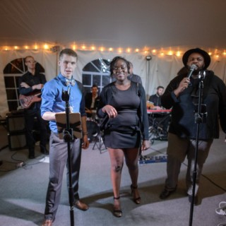 Live wedding band performing under warm string lights inside an elegant tent in Waterville Valley.