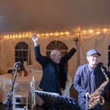 Two joyful wedding musicians performing under warm string lights in Waterville Valley, New Hampshire.