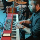 Bearded musician playing red Nord keyboard with drummer at intimate Waterville Valley wedding reception.