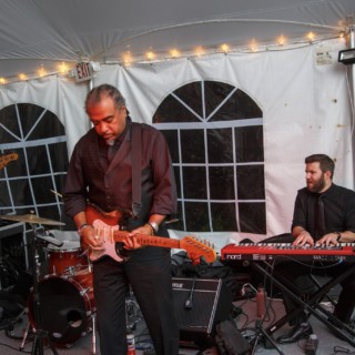 Live band performing under white tent with string lights at Waterville Valley wedding.
