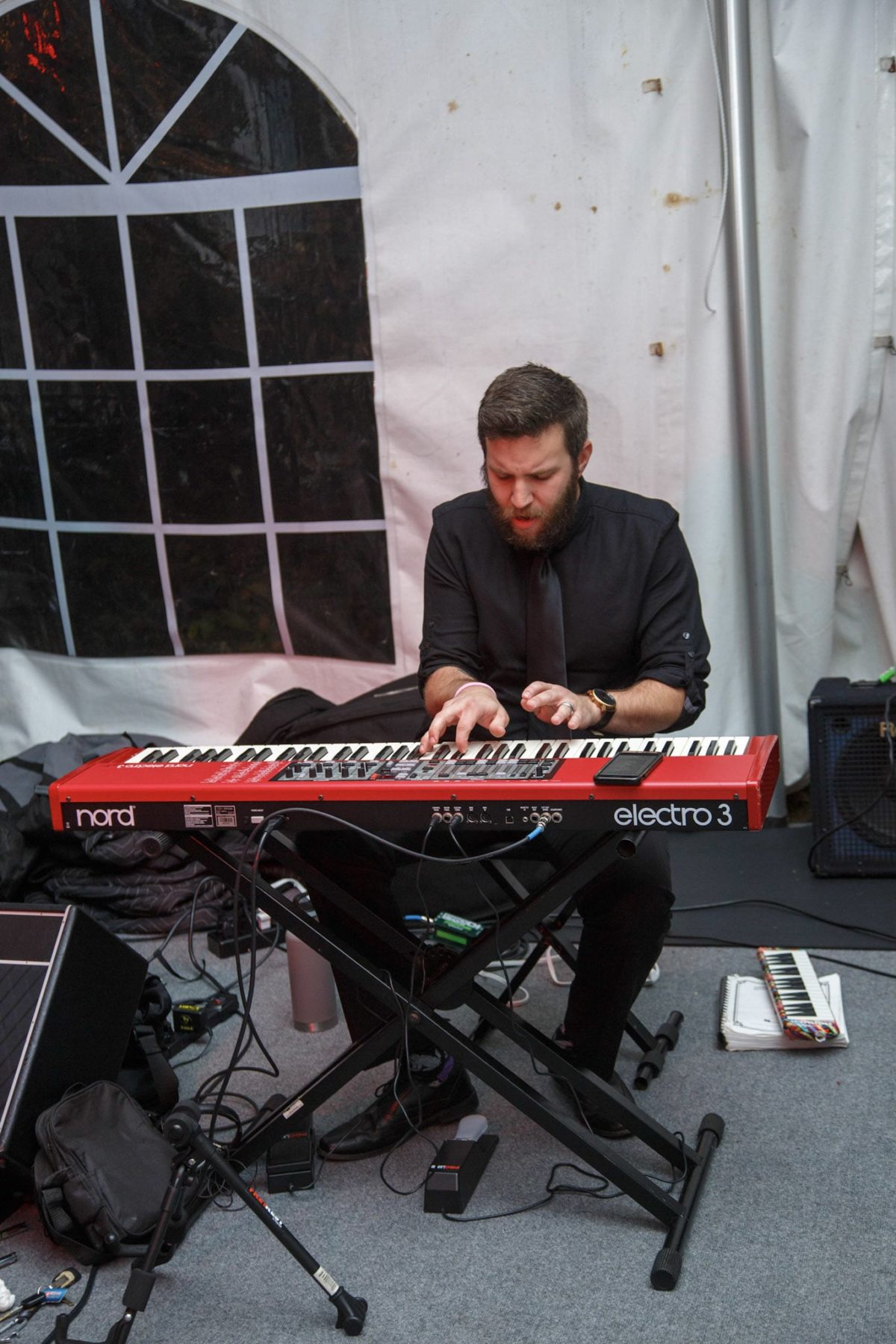 Bearded musician passionately playing red Nord keyboard under white tent at intimate live performance.