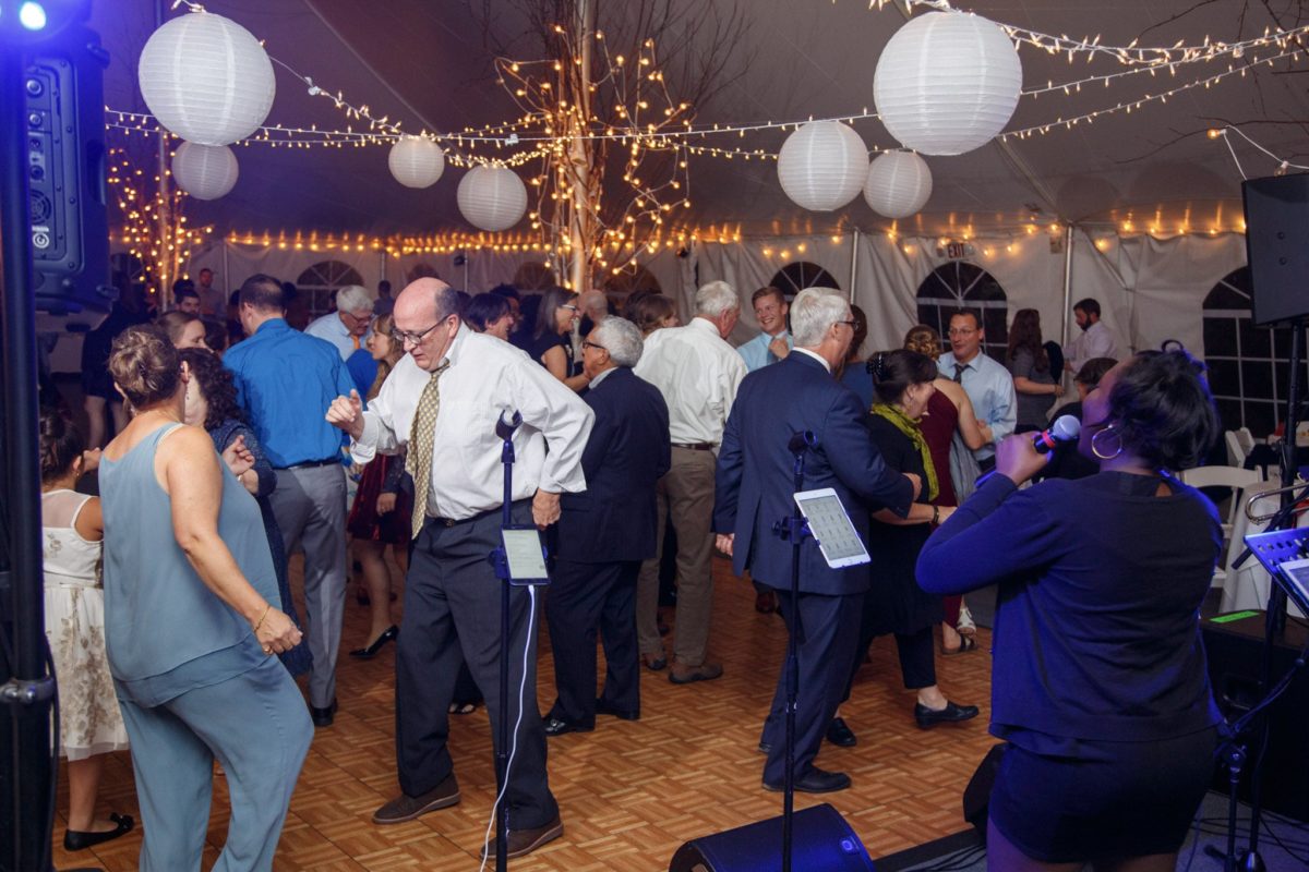 Guests dancing joyfully under lantern-lit tent with live singer at Waterville Valley wedding.