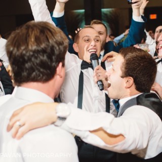Groomsmen singing and celebrating joyfully at a lively Boston Harbor wedding reception.
