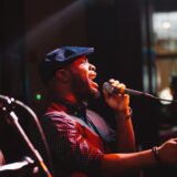Passionate male singer performing live on stage under warm lighting at a Boston music venue.