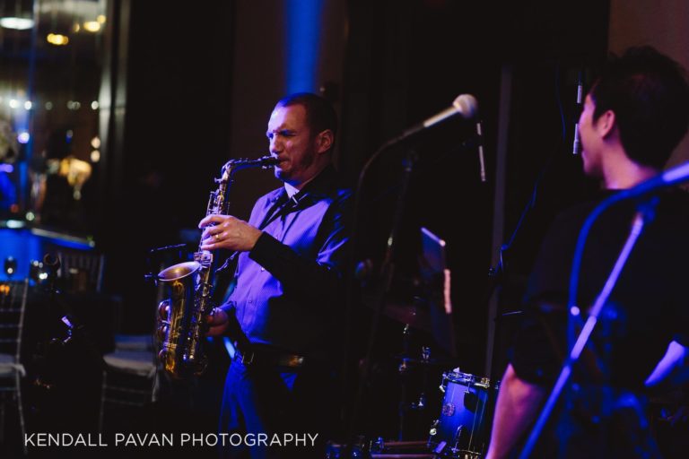 Saxophonist performing live under warm stage lights at an intimate Boston jazz event.