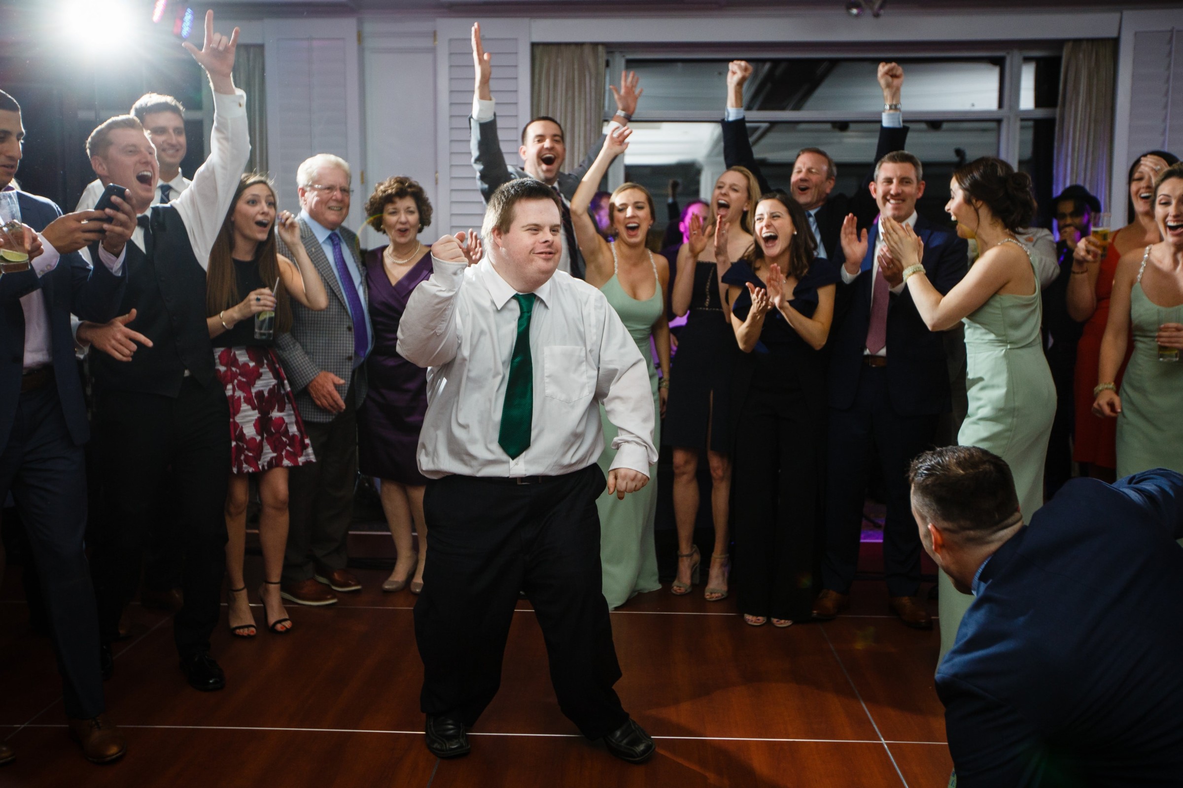 Man with Down syndrome dancing joyfully at Willowbend wedding reception surrounded by cheering guests.