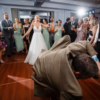 Bride laughing as guest dances energetically at lively Willowbend Country Club wedding reception.