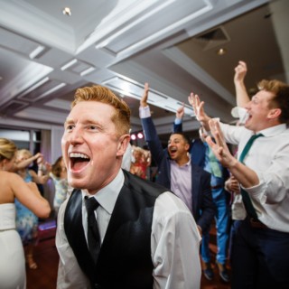 Groom laughing and dancing with guests at a lively Willowbend Country Club wedding reception.