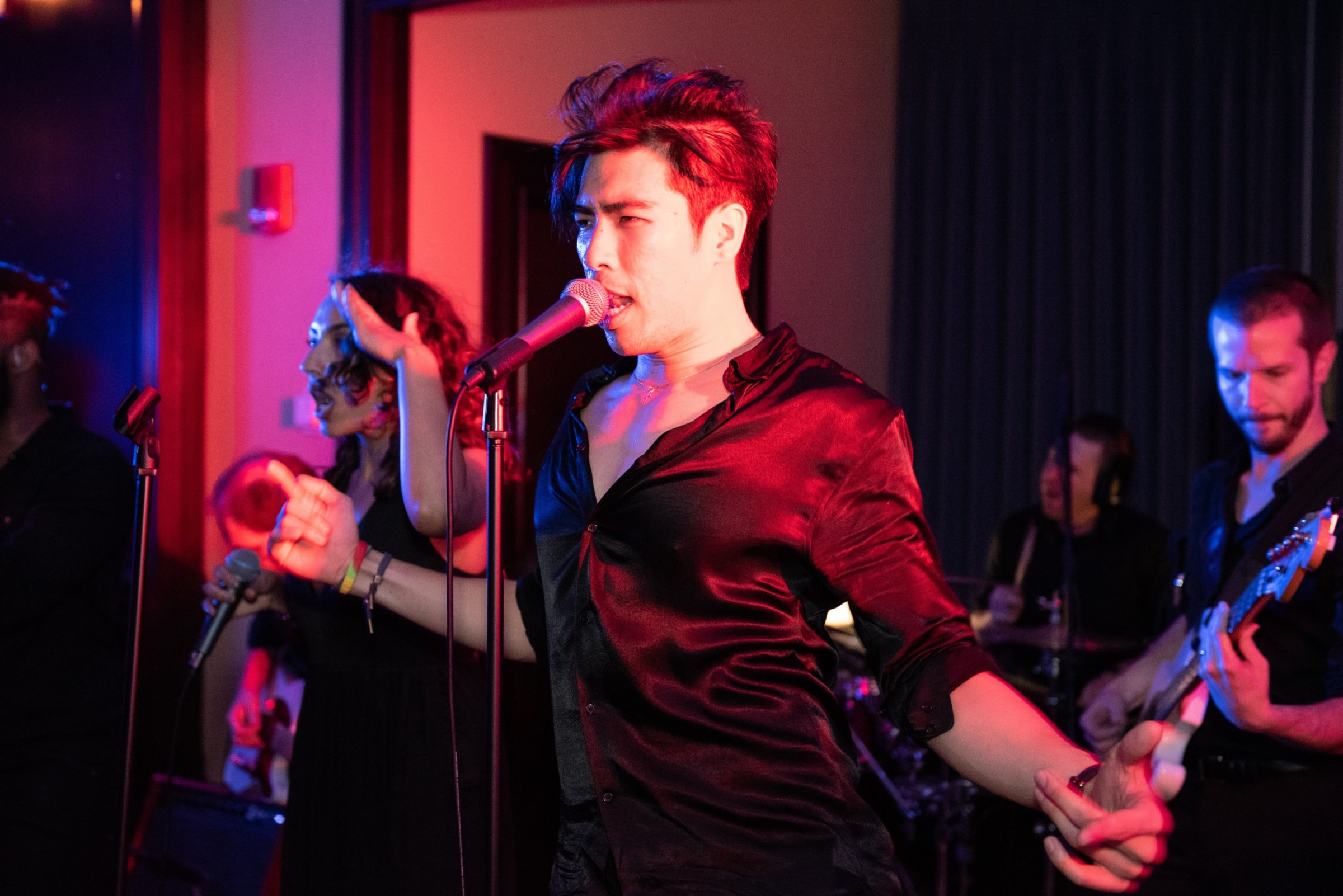 Lead singer and band performing passionately under colorful stage lights at an intimate indoor concert.