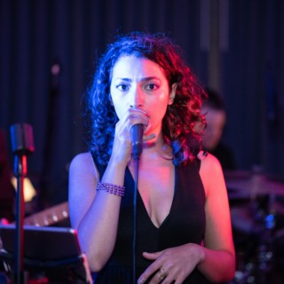 Female singer performing live on stage under vibrant blue and magenta lights.