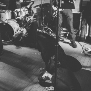 Black-and-white photo of emotional live music performance with passionate vocalist kneeling on stage.