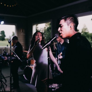 Live wedding band performing indoors on Thompson Island with vocalists singing under warm stage lights.