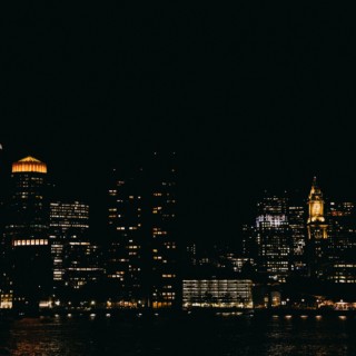 Boston skyline at night glowing over the harbor with city lights reflecting on calm water.