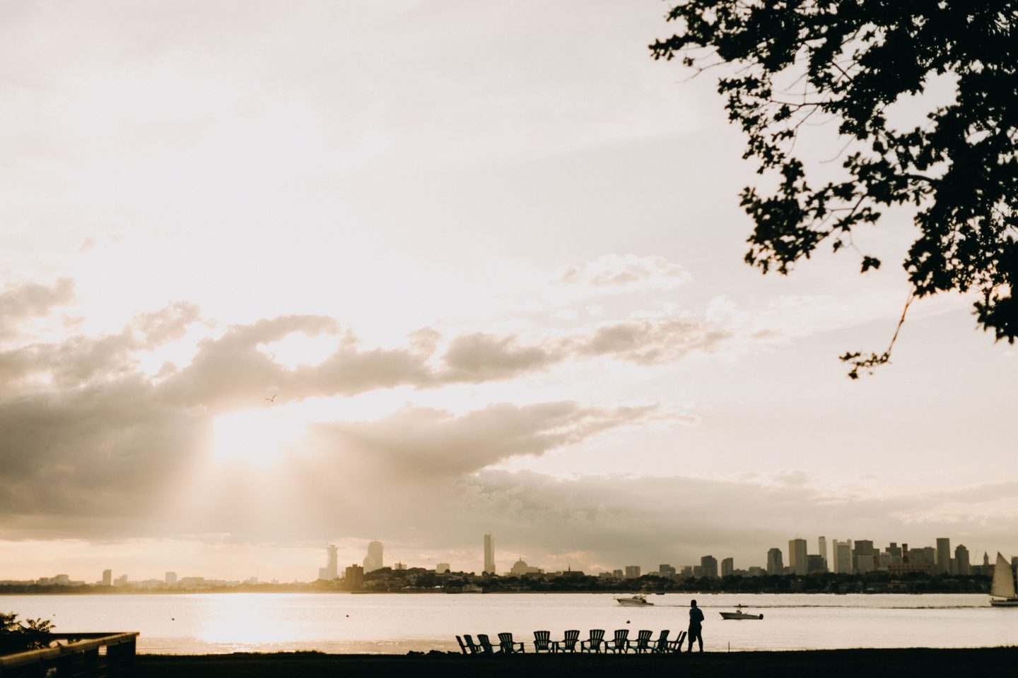 Golden sunset over Boston Harbor with skyline silhouette, calm water, and a peaceful waterfront scene.
