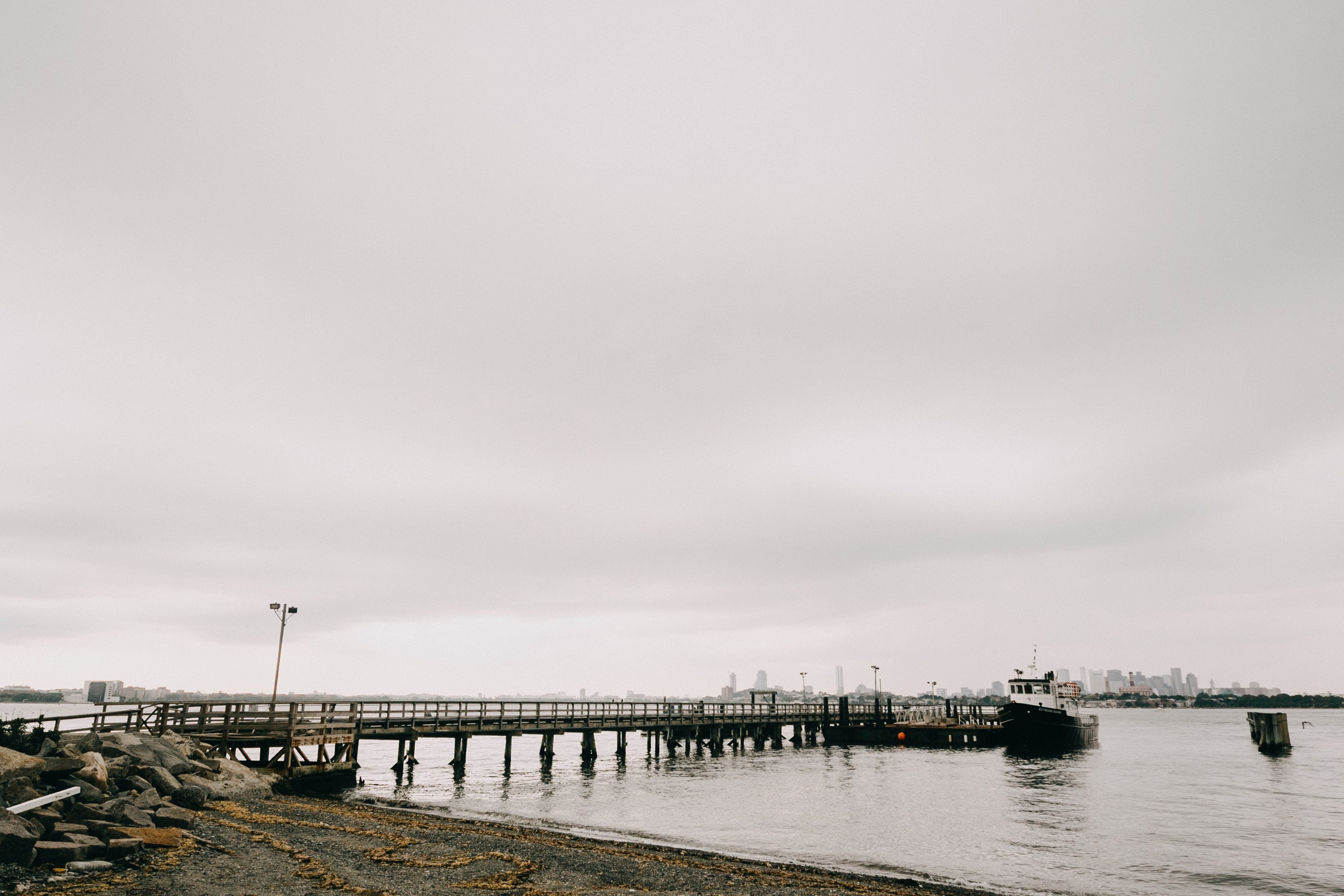 Peaceful wooden pier and boat on calm gray waterfront with distant Boston skyline.