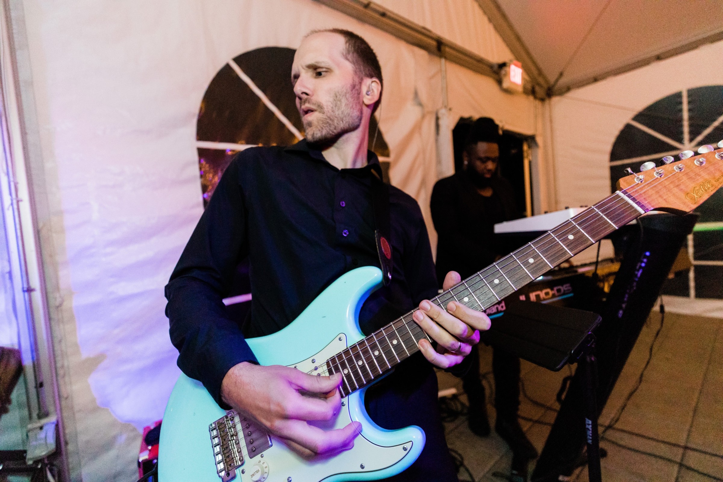 Guitarist performing passionately with blue electric guitar under glowing wedding tent lights in Wellesley, MA.
