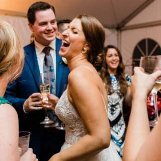 Bride and groom laughing with guests during joyful Elm Bank wedding reception in Wellesley, Massachusetts.