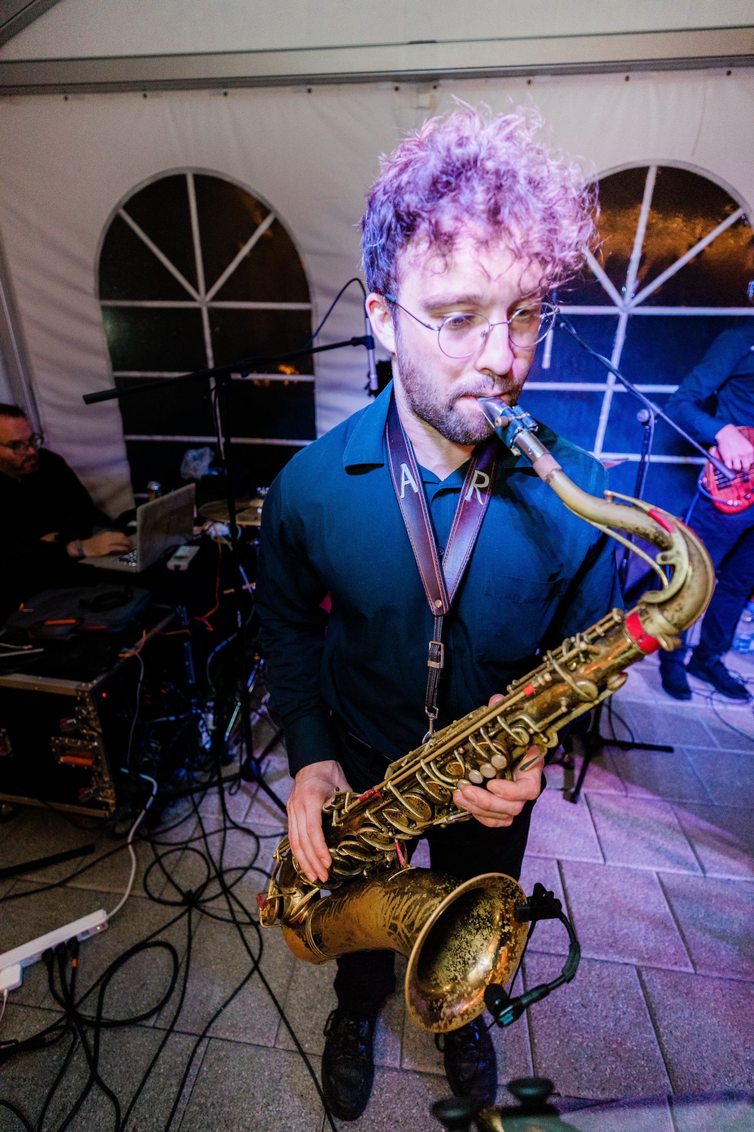Focused jazz saxophonist performing live under colorful stage lights at an outdoor event.