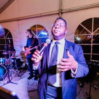 Wedding band performing under white tent in Wellesley with energetic singer and colorful stage lighting.