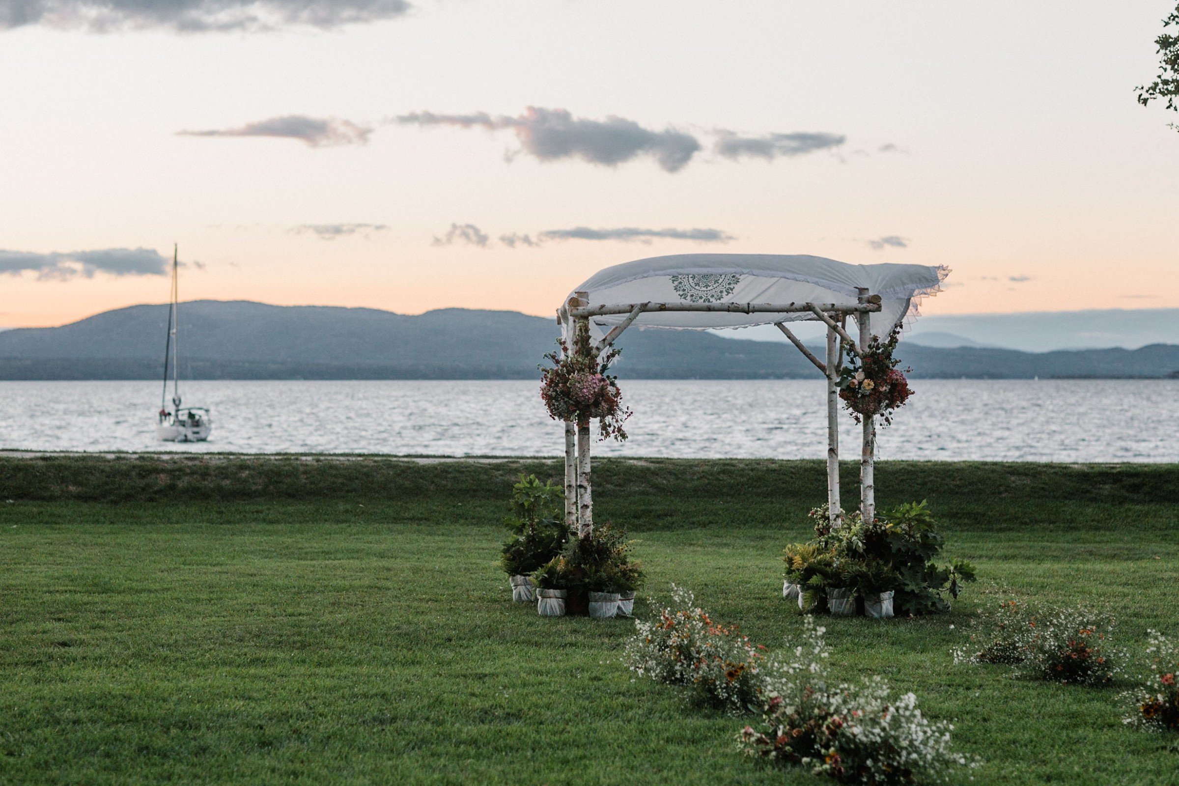 Rustic birch wedding arch by a serene Vermont lake at sunset with floral accents.