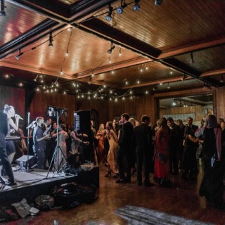 Elegant wedding reception with live band, dancing guests, and warm wooden hall lighting in Vermont.