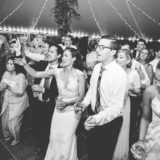 Bride and groom dancing joyfully under twinkling lights at Twin Lake Village wedding reception.