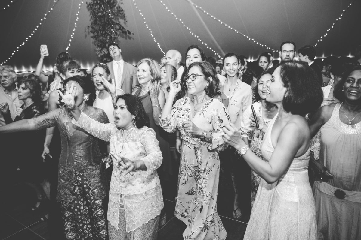 Joyful wedding guests dancing and singing under glowing string lights in New London, New Hampshire.