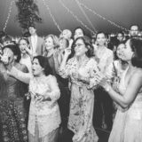 Joyful wedding guests dancing and singing under glowing string lights in New London, New Hampshire.