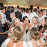 Bride and bridesmaids dancing joyfully under glowing string lights at Twin Lake Village wedding reception.