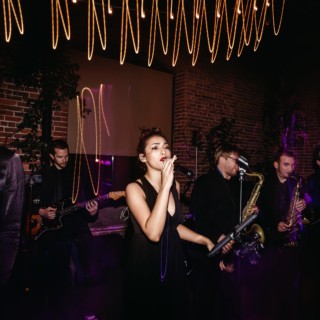 Live band performing with singers and brass section under warm lighting at Dover NH venue