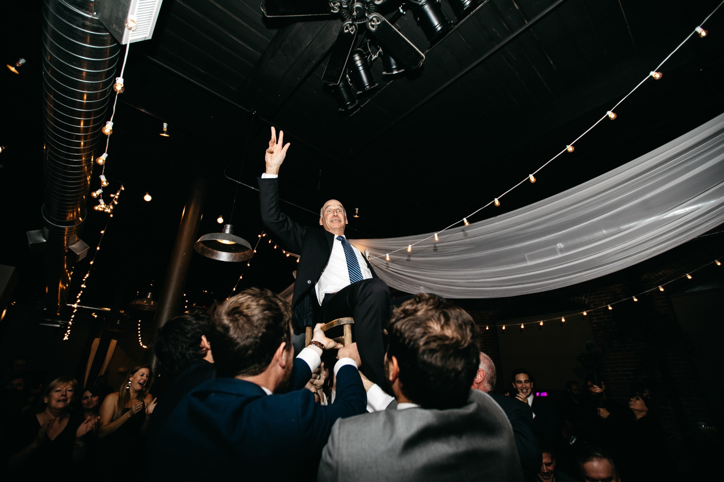 Groom lifted on chair during joyful Rivermill wedding celebration in Dover, New Hampshire.