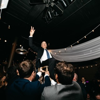 Groom lifted on chair during joyful Rivermill wedding celebration in Dover, New Hampshire.