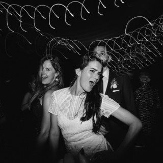 Bride joyfully dancing with friends under glowing lights at Rivermill wedding celebration.