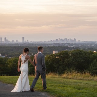 Bride and groom walking hand in hand at sunset overlooking Boston skyline at Granite Links.