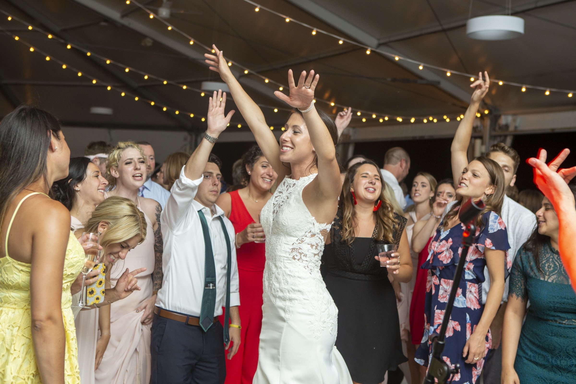 Bride dancing surrounded by guests under warm string lights at Granite Links wedding in Quincy.