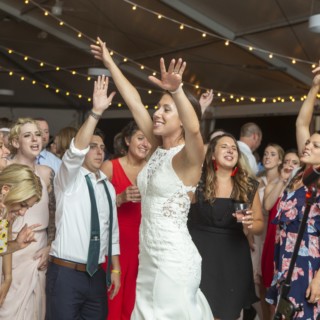 Bride dancing surrounded by guests under warm string lights at Granite Links wedding in Quincy.