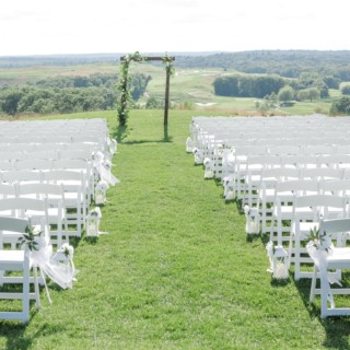 Outdoor wedding ceremony with white chairs, floral arch, and scenic hillside backdrop in Quincy, MA.