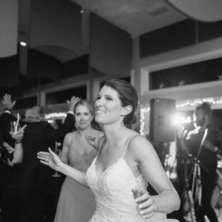 Joyful bride dancing with guests during lively black-and-white West Dennis Yacht Club wedding celebration.
