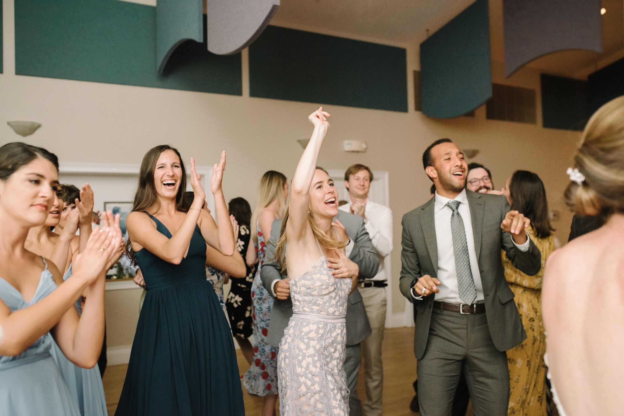 Guests dancing and laughing at a lively wedding reception in warm indoor lighting.