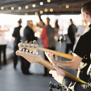 Guitarist performing at elegant evening event with guests mingling under warm string lights.