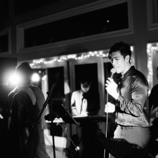 Black and white photo of live band performing passionately under dramatic evening lighting indoors.