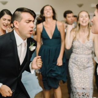 Bride and groom joyfully dancing surrounded by guests at lively West Dennis Yacht Club wedding.