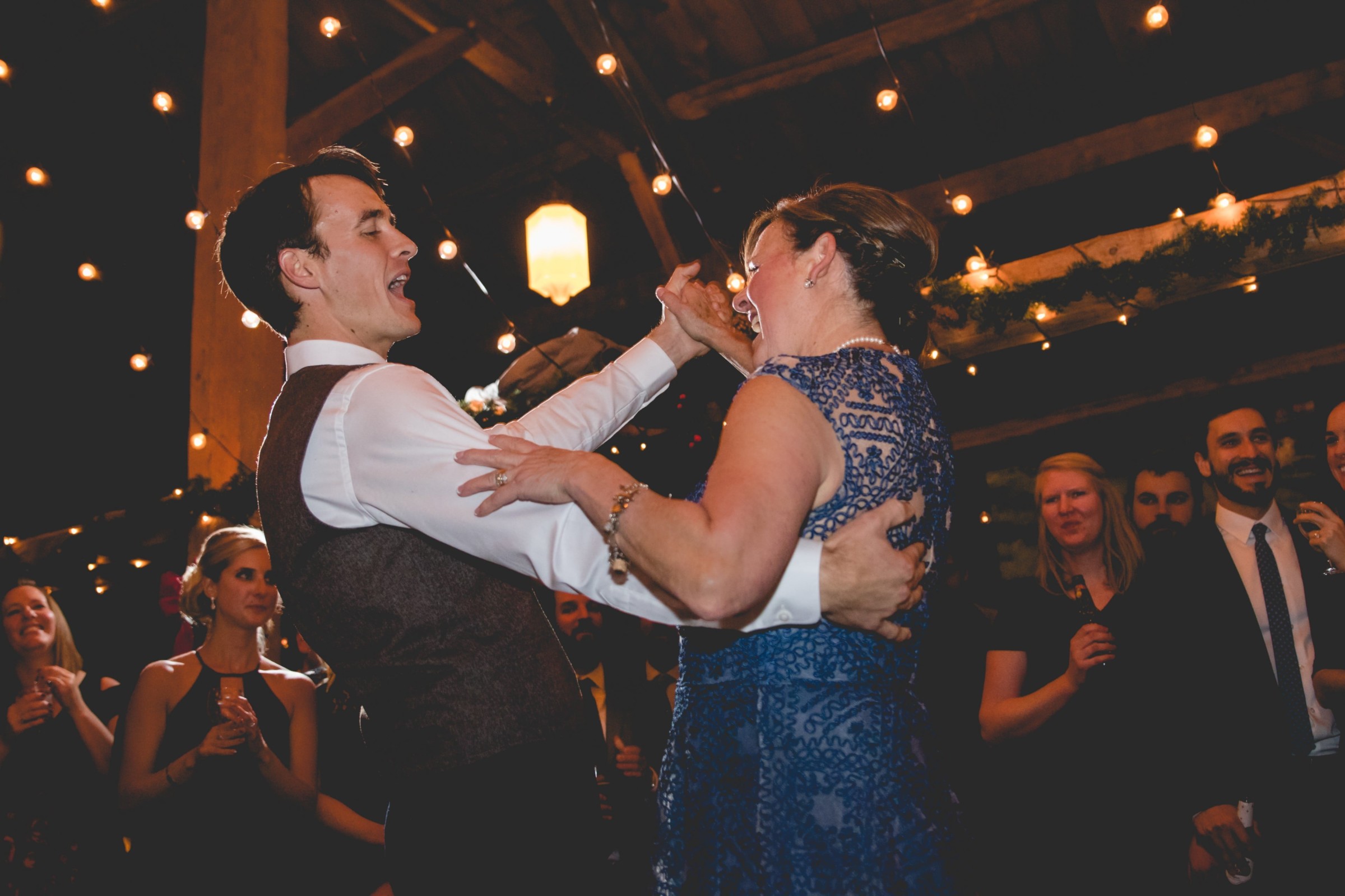Groom and mother dancing joyfully under warm string lights at Stone Mountain Arts Center wedding.