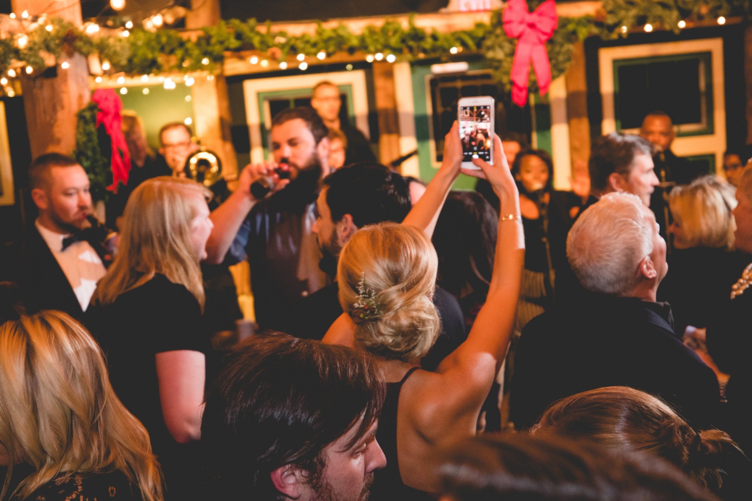Guests celebrating indoors with live music, warm lights, and festive holiday decorations.