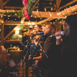 Live holiday band performing at rustic Stone Mountain Arts Center in warm festive lighting.